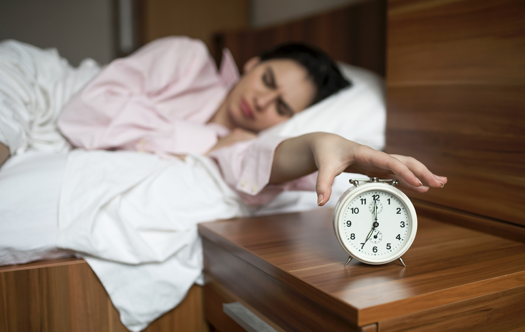 AltaMed woman reaching for alarm clock in bed
