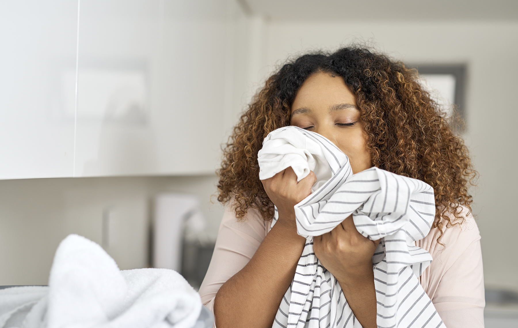 AltaMed woman taking fresh sheets out of dryer and smelling them