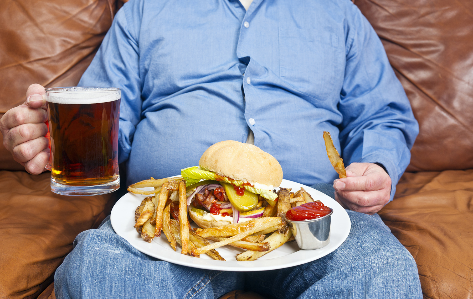 AltaMed chubby man sitting on couch with burger fries and beer
