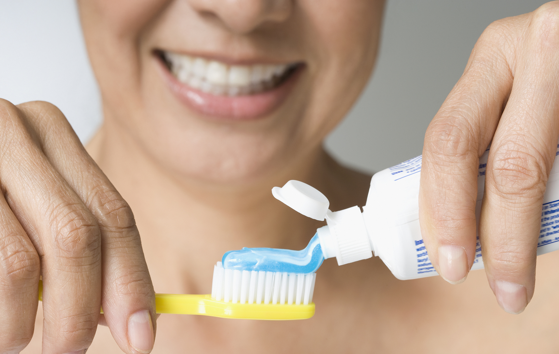 AltaMed woman smiling putting toothpaste on yellow toothbrush